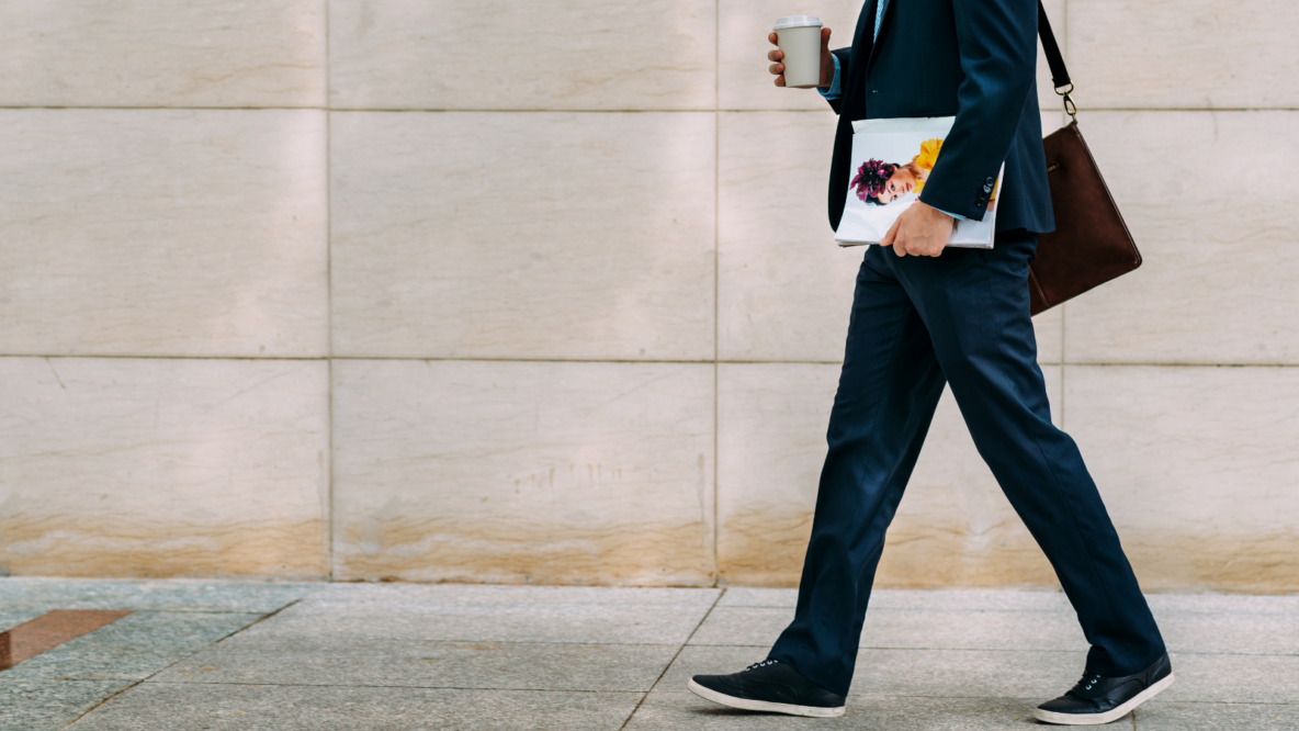 business man walking with magazine and coffee.png